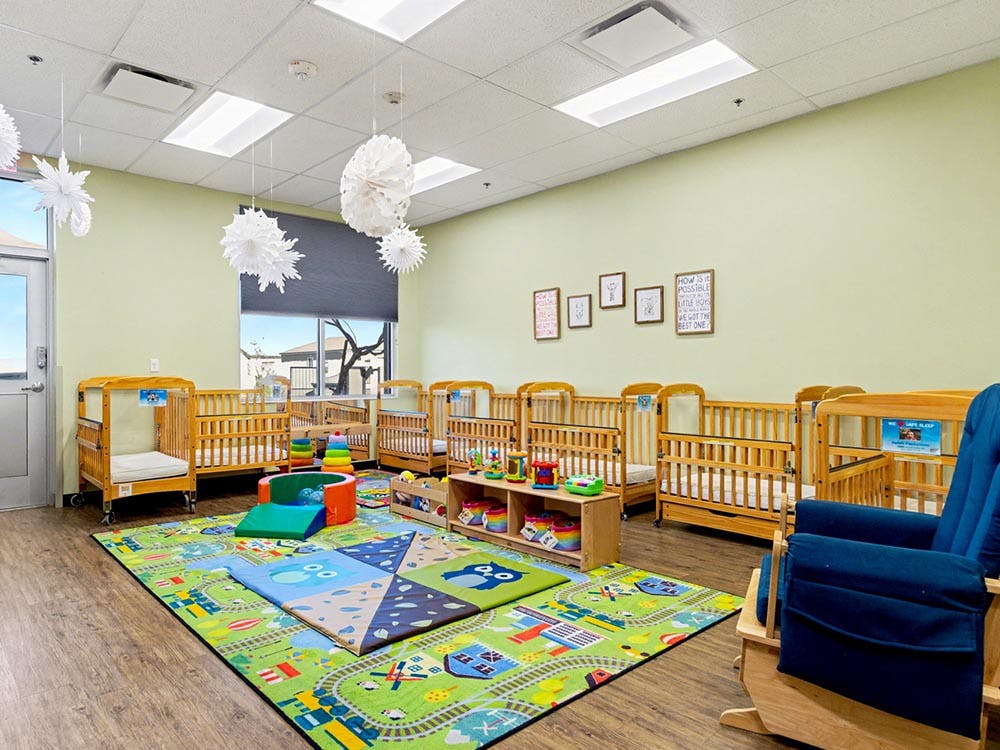 Cribs in a daycare room with a play mat, toys, and a rocking chair