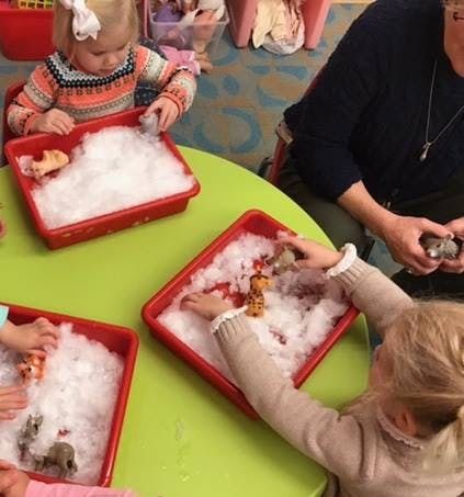 Children playing with animal toys in trays of white fluffy material