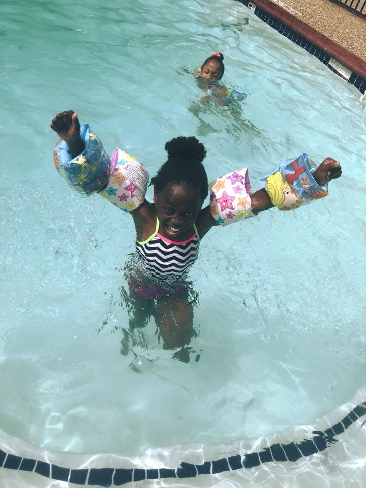 Child in a pool wearing arm floats, another child in background