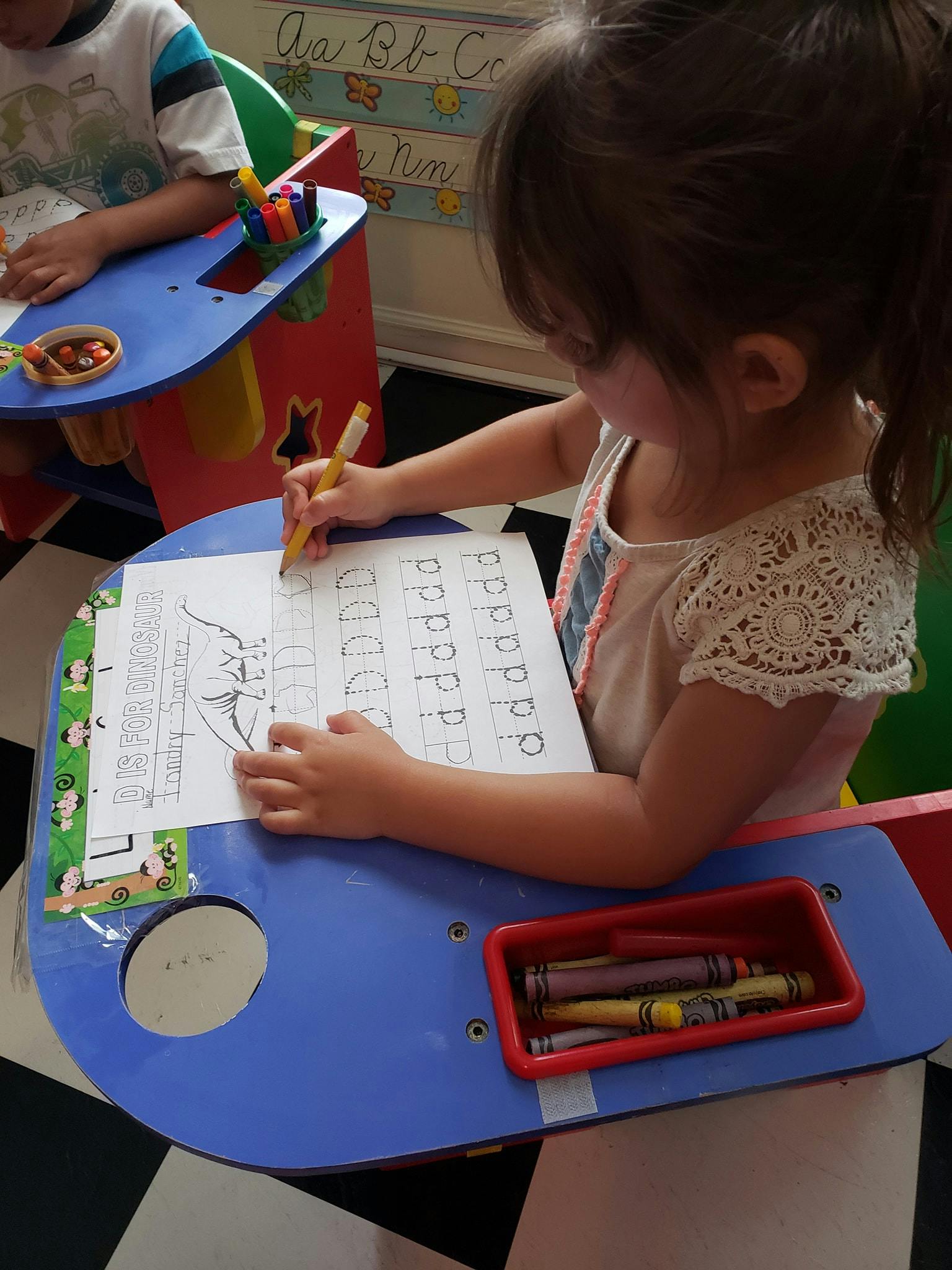 Child tracing letters on a worksheet at a desk