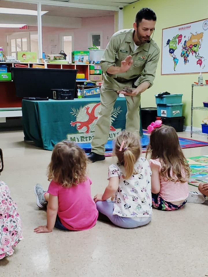 Adult showing small animal to children sitting on the floor