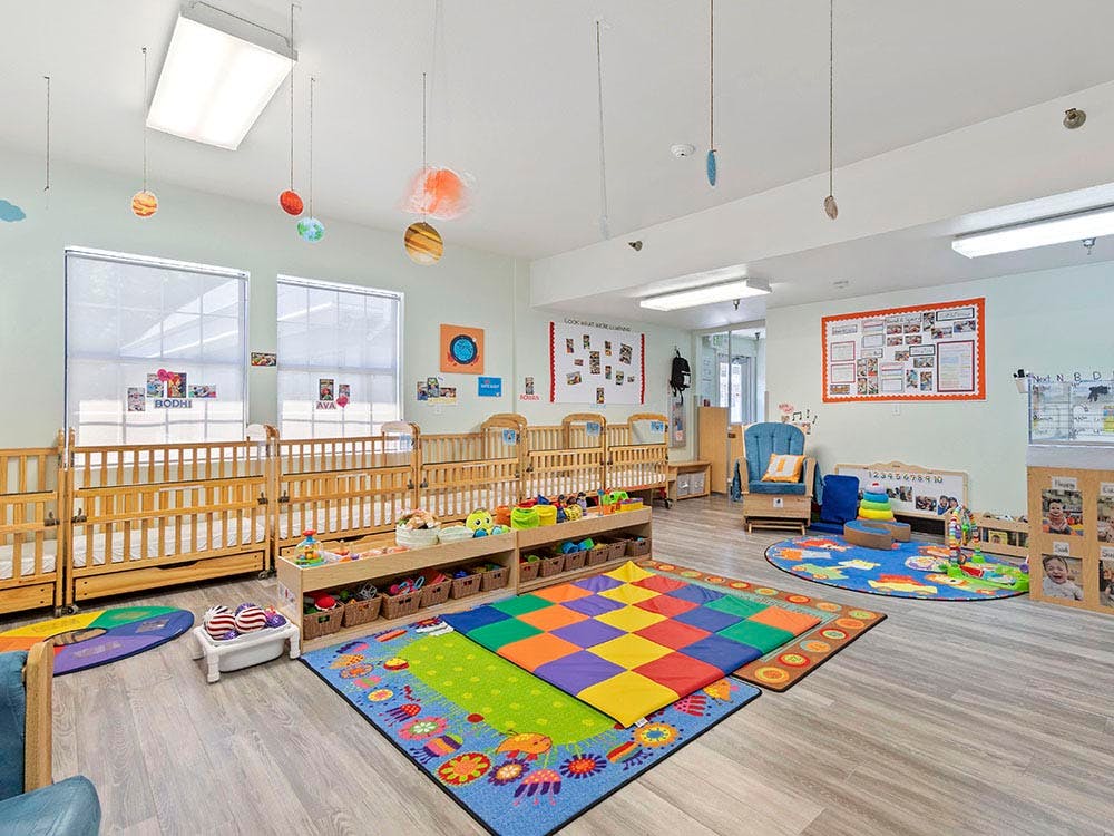 A colorful daycare room with cribs, playmats, and toys