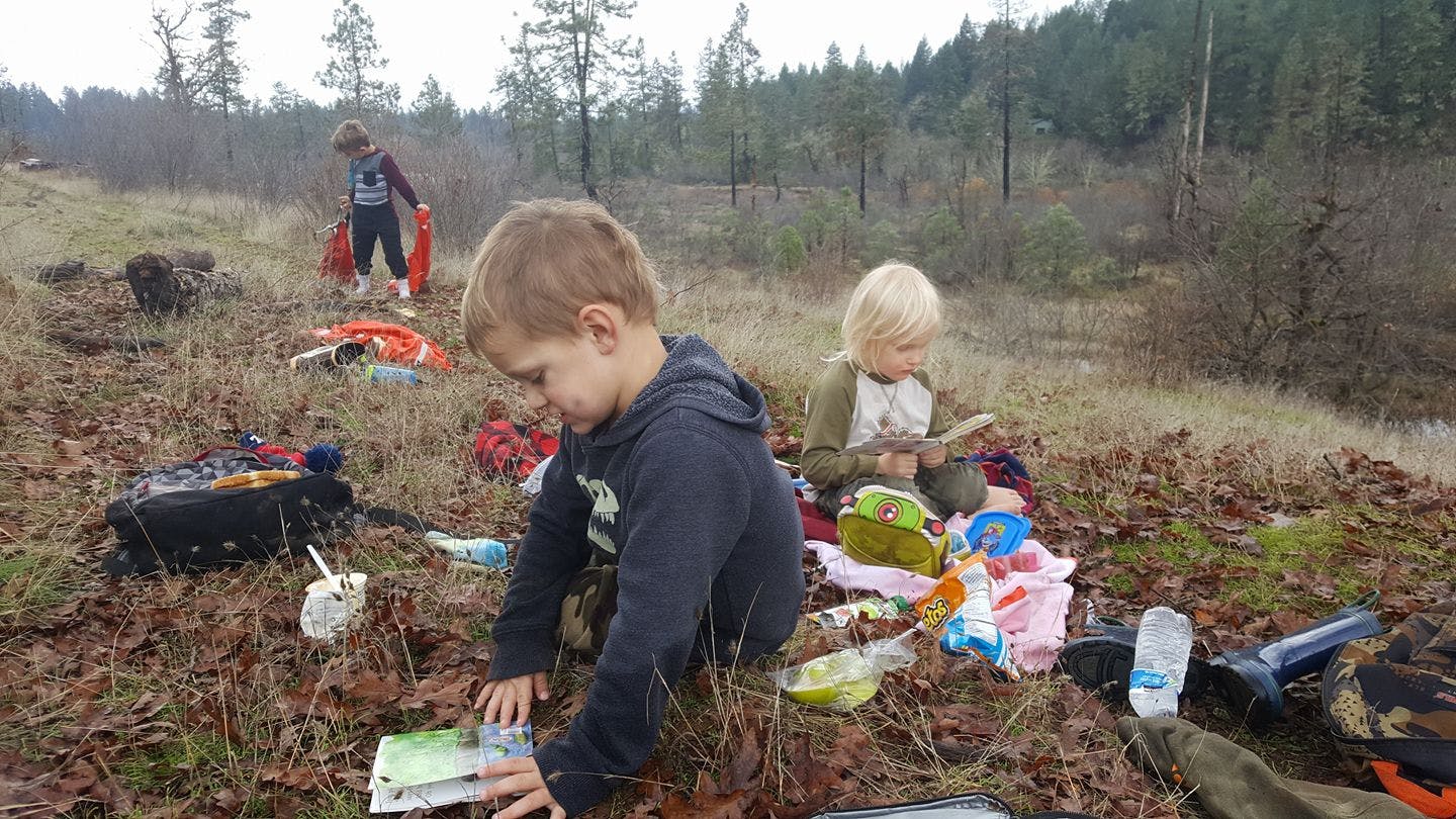 Child looking at a book outdoors with another child nearby