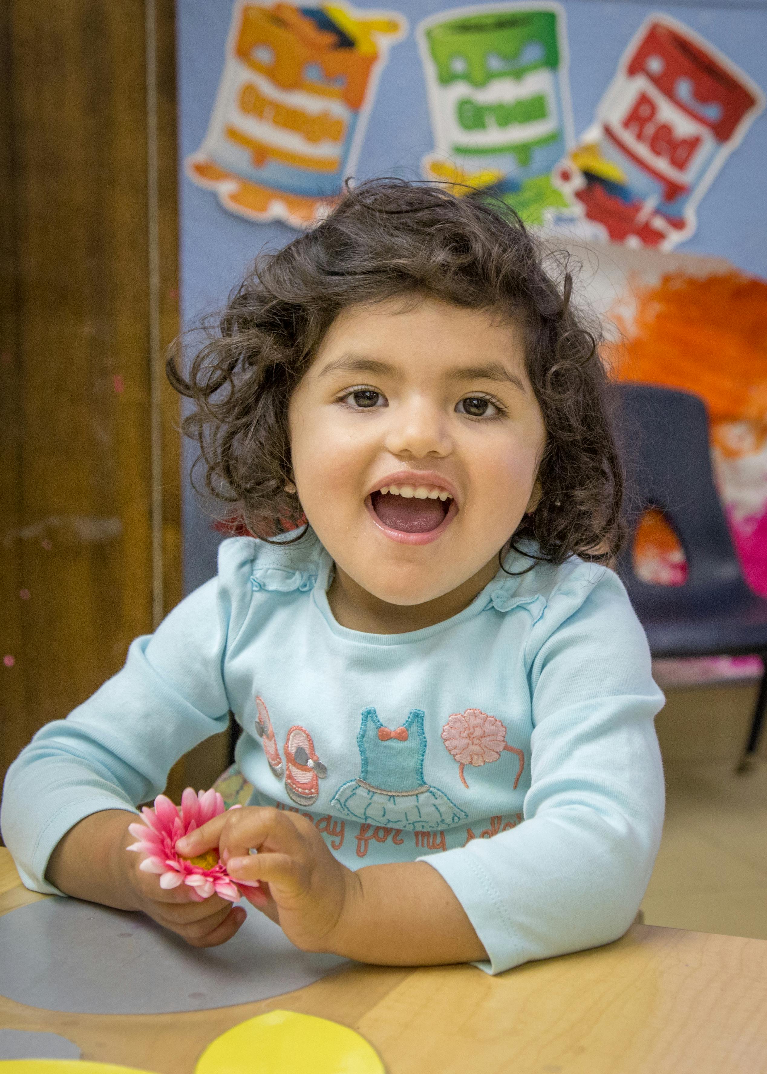 Child holding a pink flower at a table