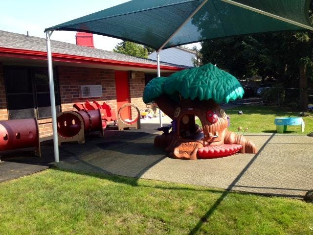 Outdoor play area with a tree-shaped playhouse and red tunnels under a canopy