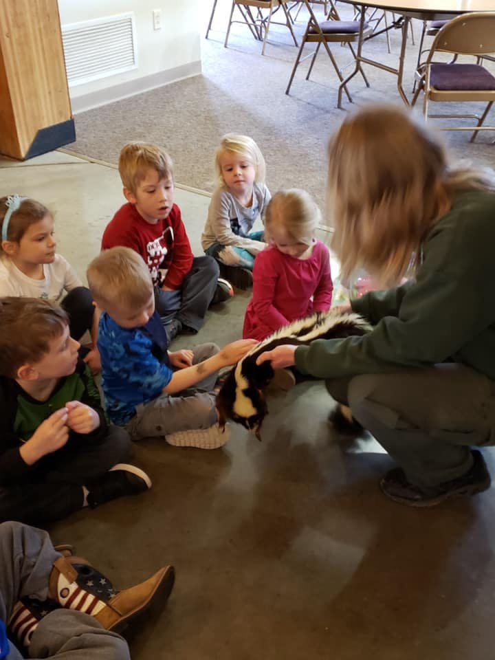 Adult and children sitting on floor petting a skunk