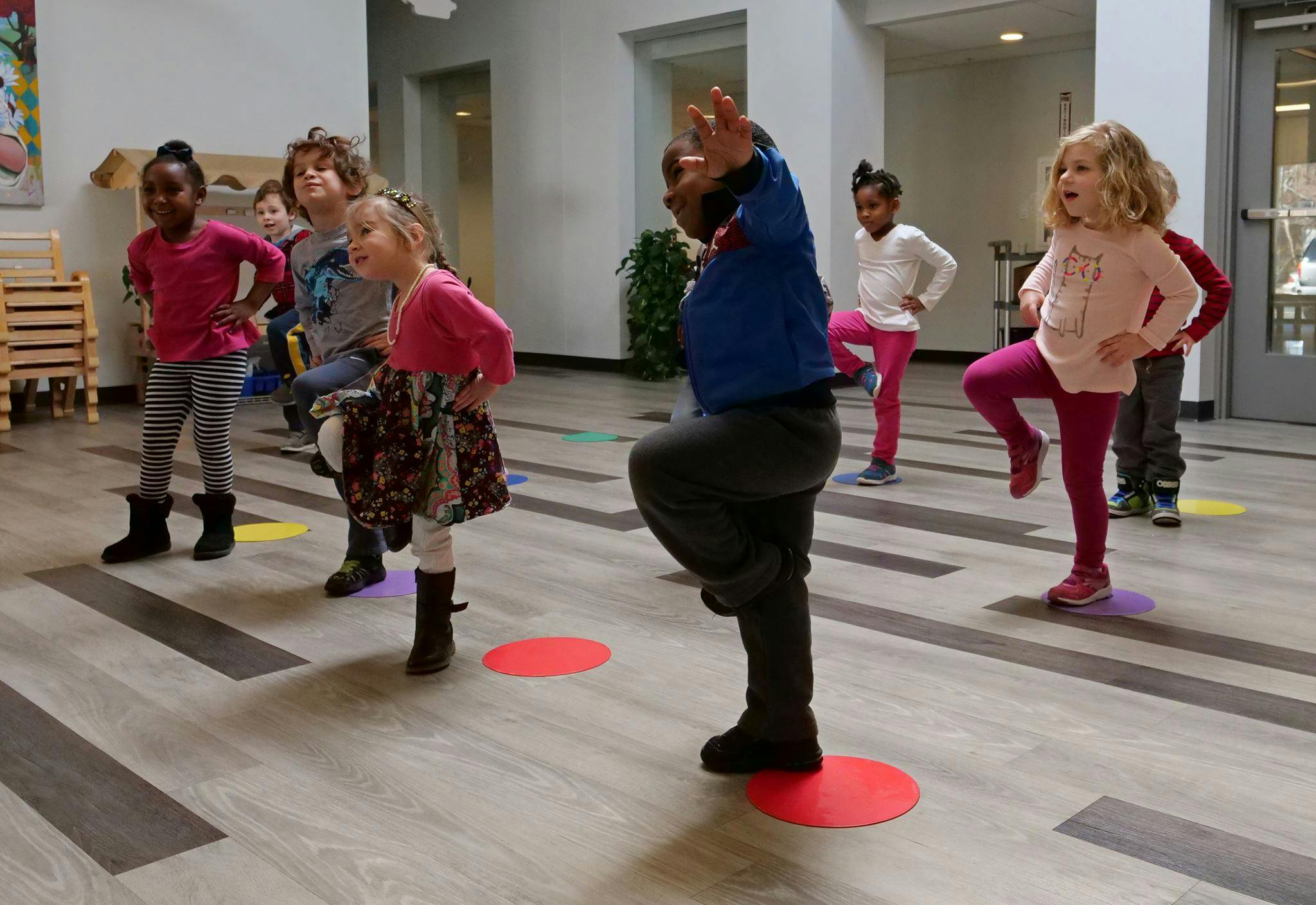 Children standing on colorful circles, some balancing on one leg