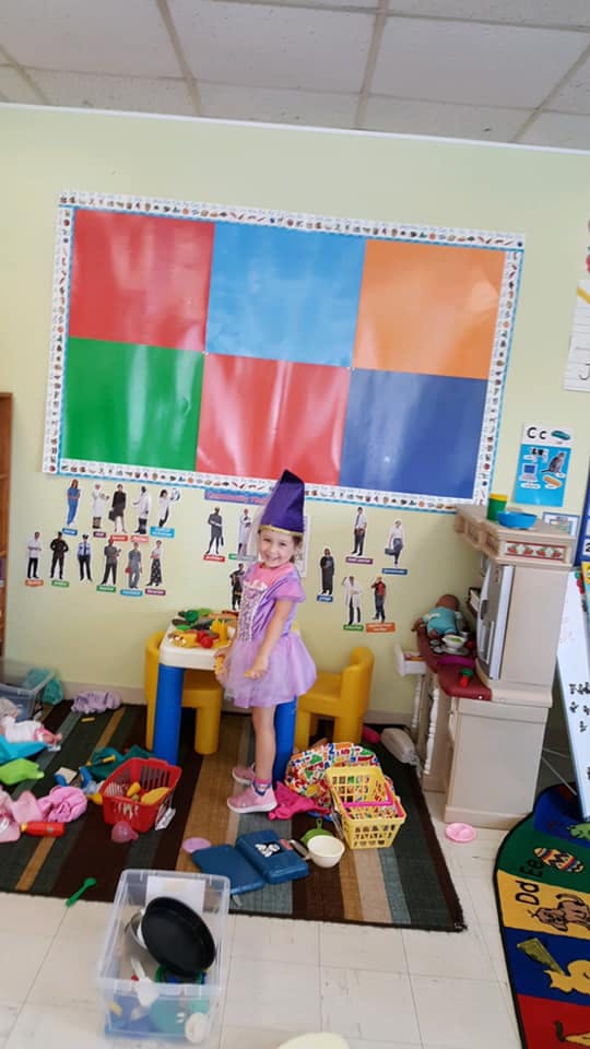 Child in a purple dress and hat standing in a classroom