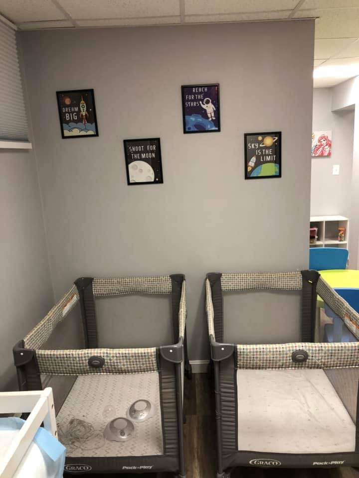 Two playpens in a room with space-themed pictures on the wall