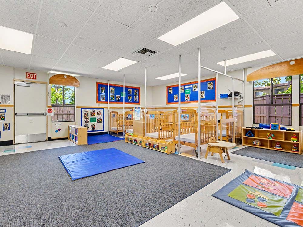 Empty infant room with multiple cribs, a blue mat, and an exit door