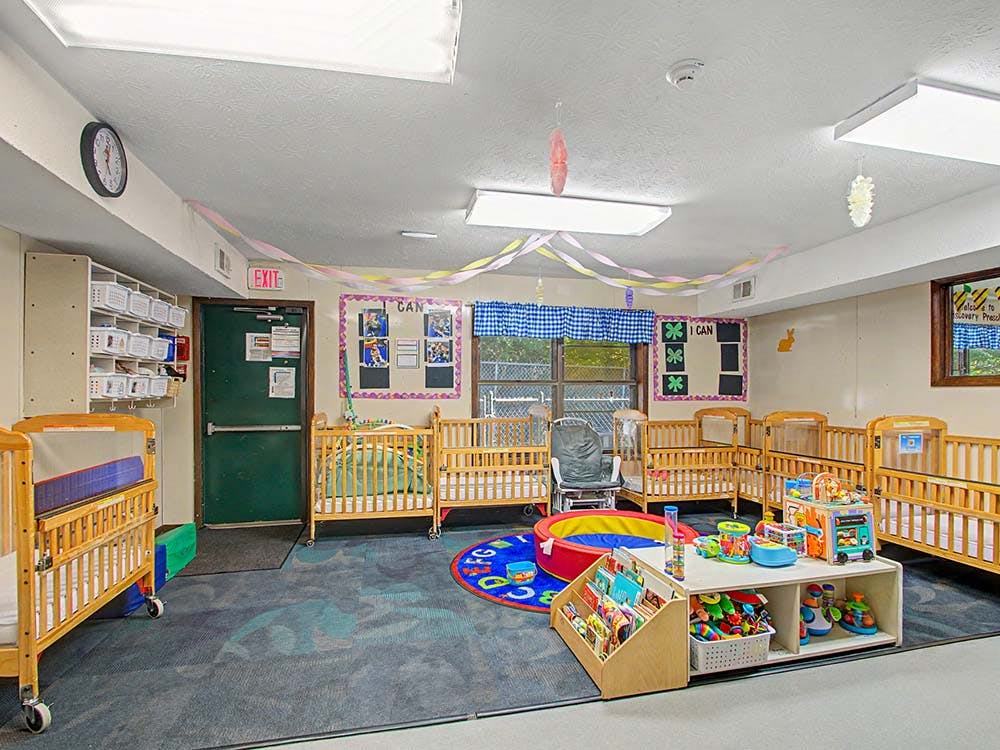 Cribs and play area in a brightly lit daycare or nursery room