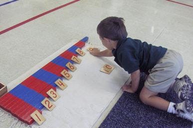 Child kneeling on floor, placing number tiles next to counting rods