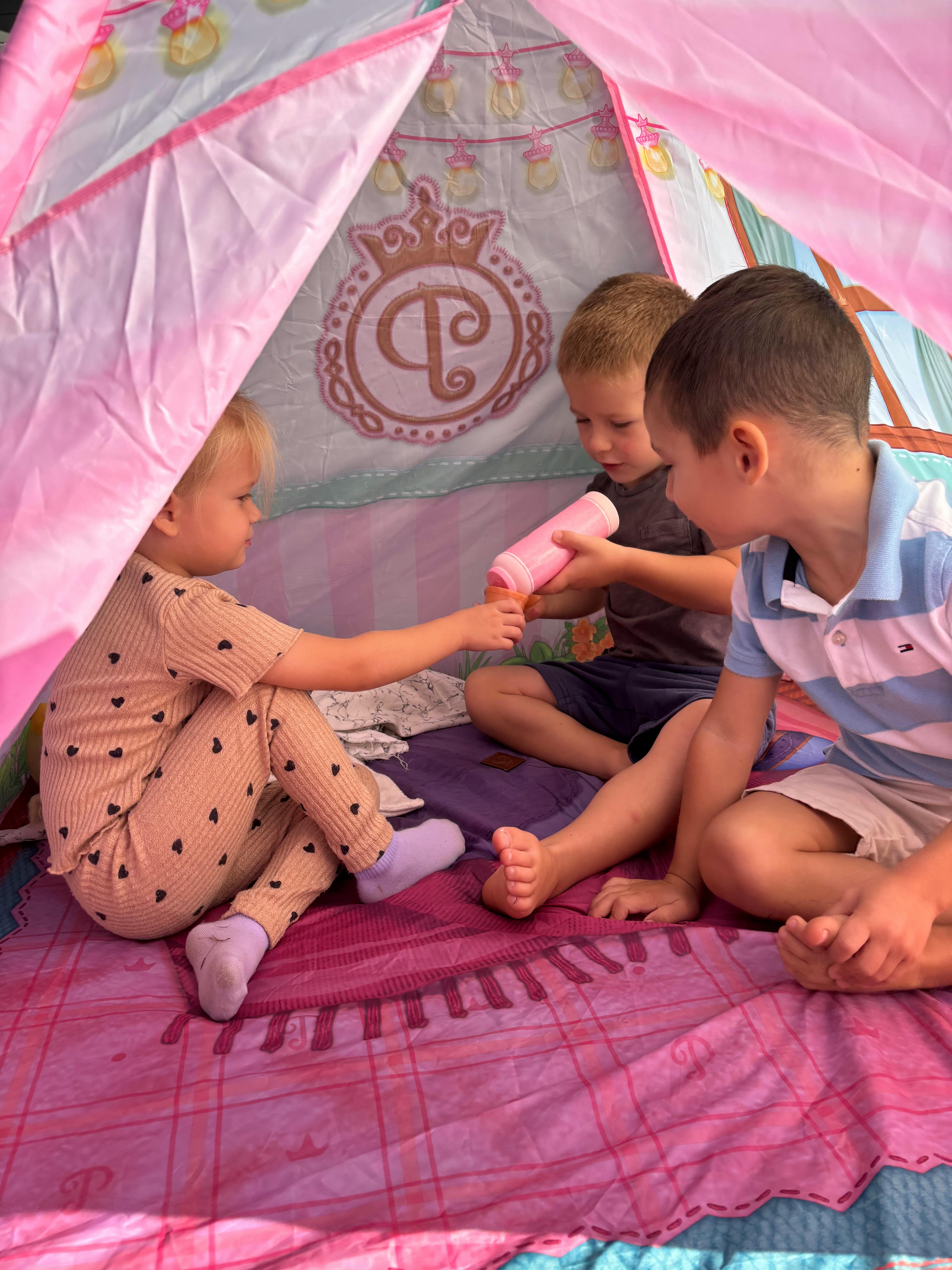 Three children playing inside a pink tent
