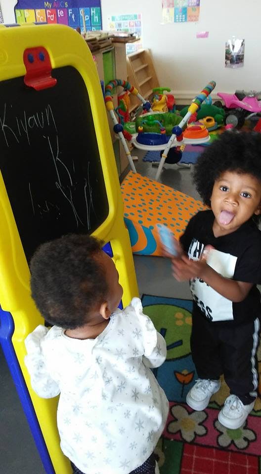 Two children standing near a yellow easel in a playroom