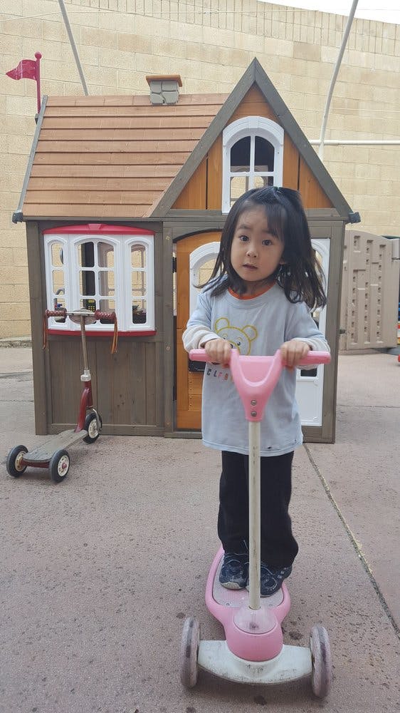 Child standing on a pink scooter in front of a playhouse