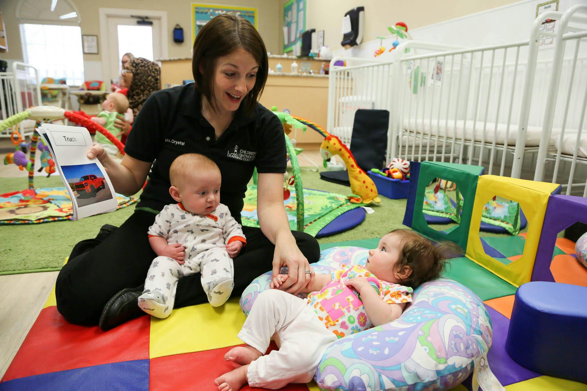 Person reading a book to two babies in a play area