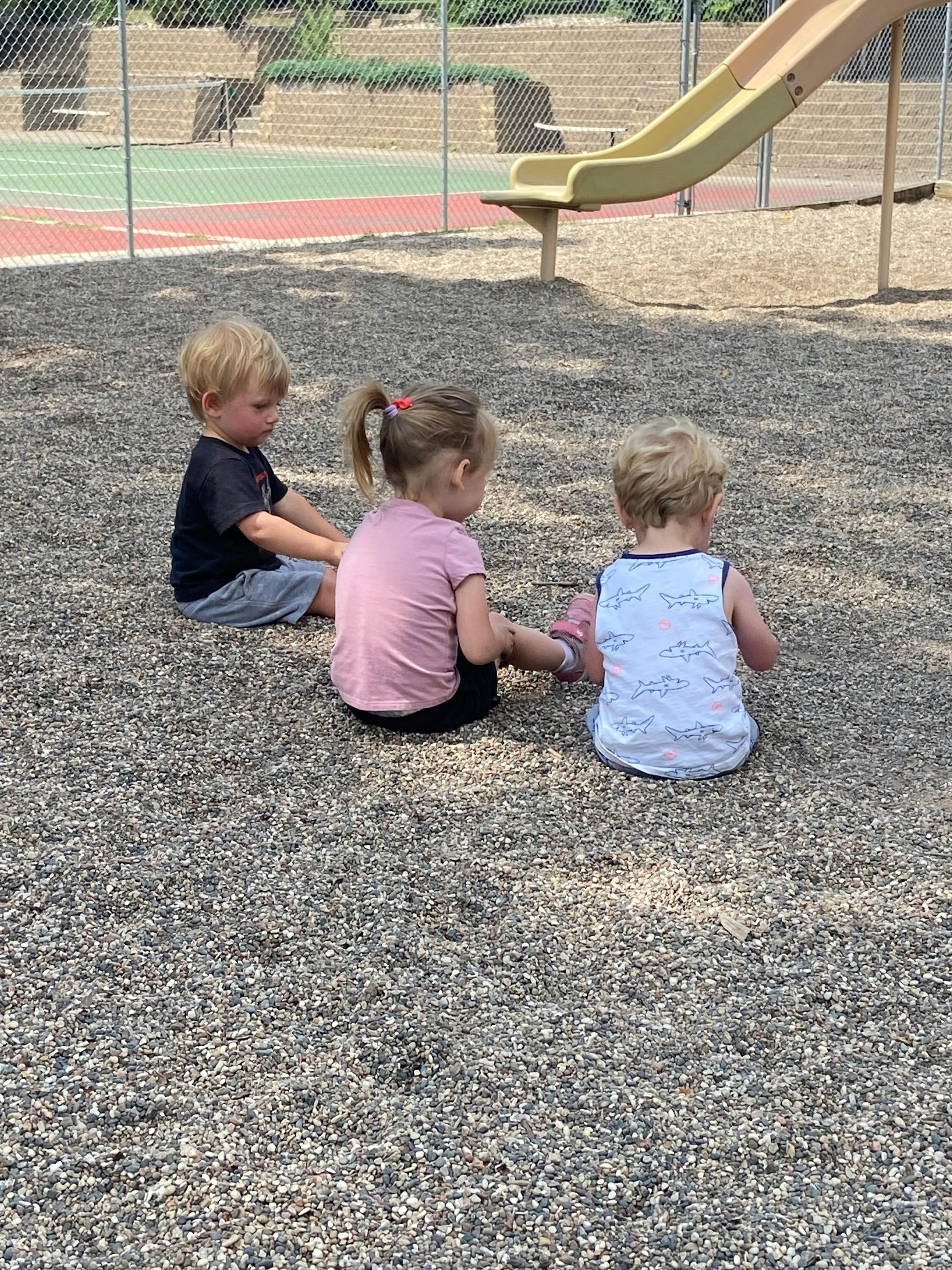 Three children sitting on a gravel playground
