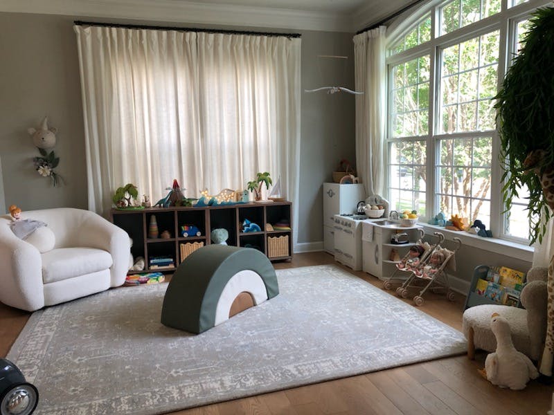 Playroom with a white armchair, toy storage, and large windows