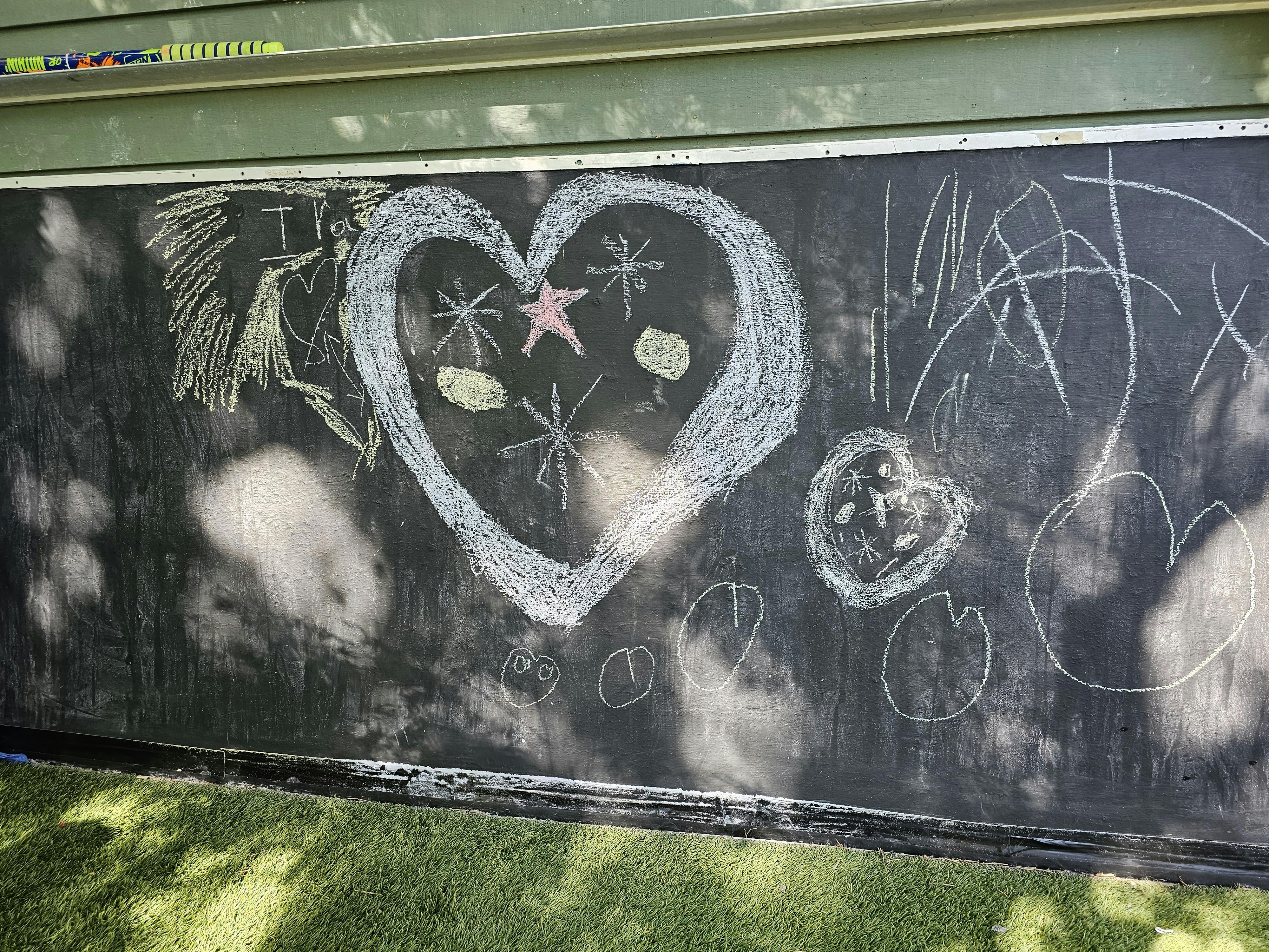 Chalk drawings of hearts and stars on a black outdoor wall