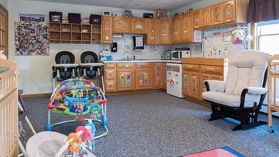 Childcare room with kitchen cabinets, high chairs, and baby play equipment