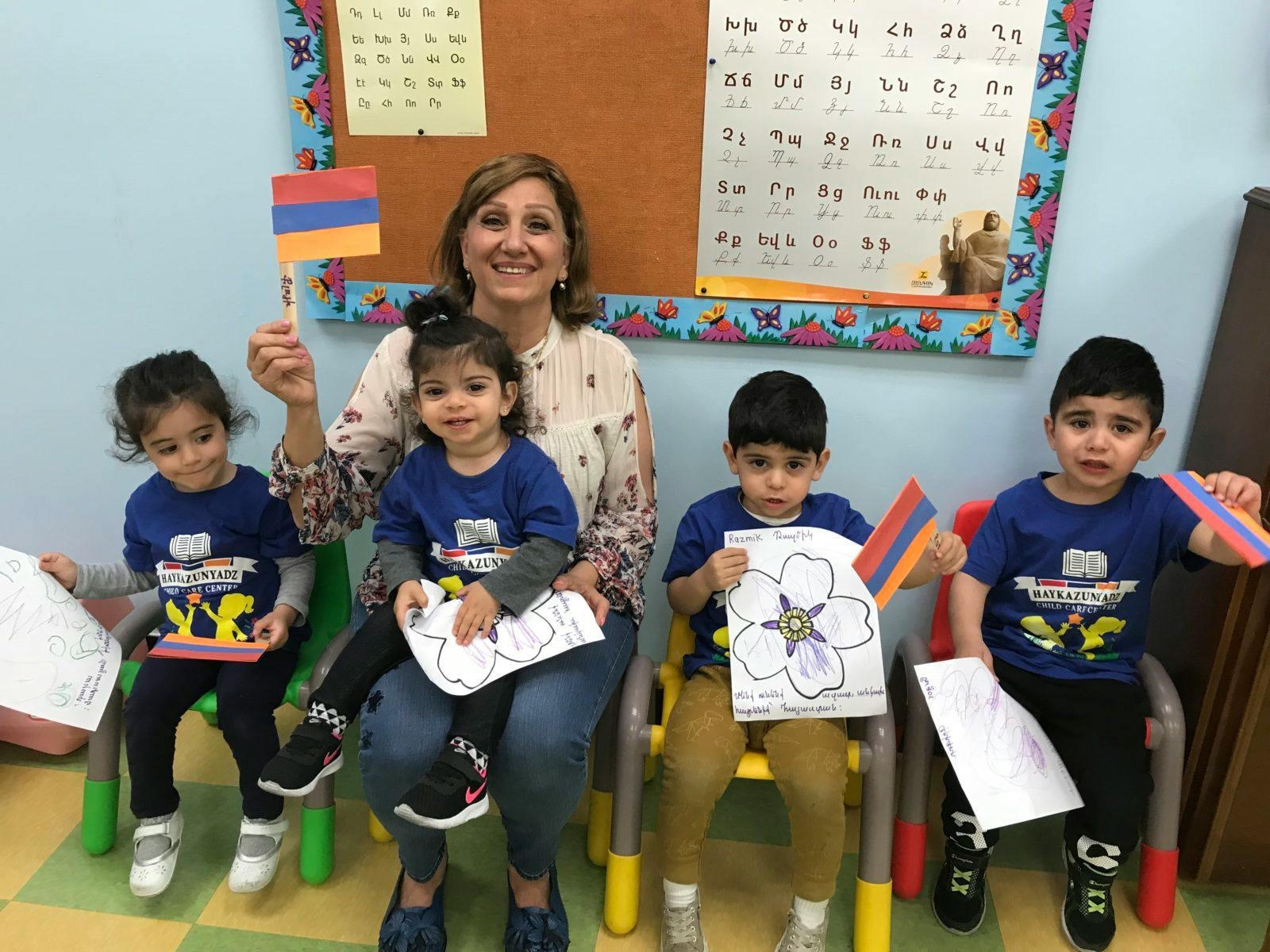 Adult and four children holding flags and drawings in a classroom
