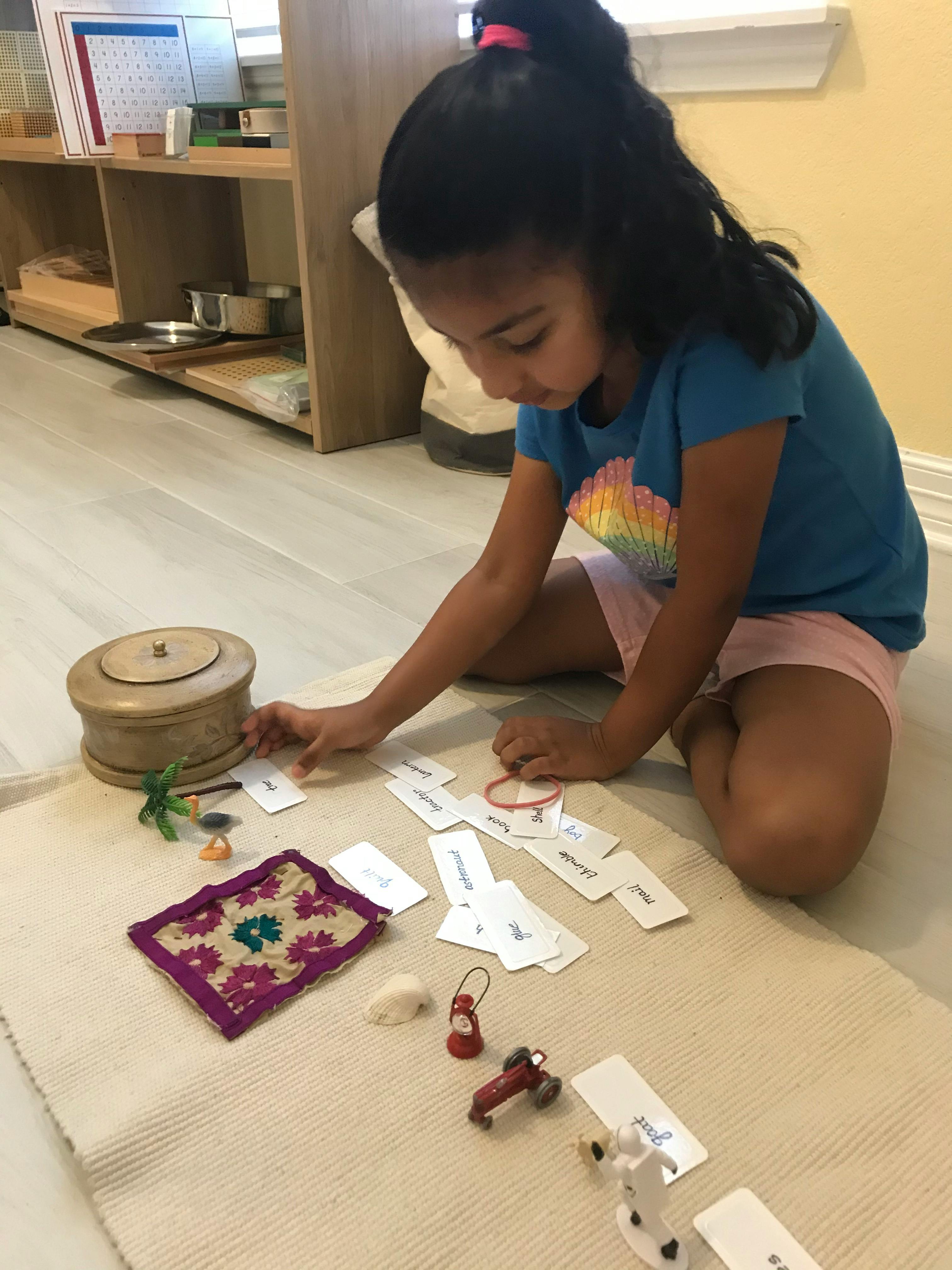 Child on floor playing with small objects and word cards