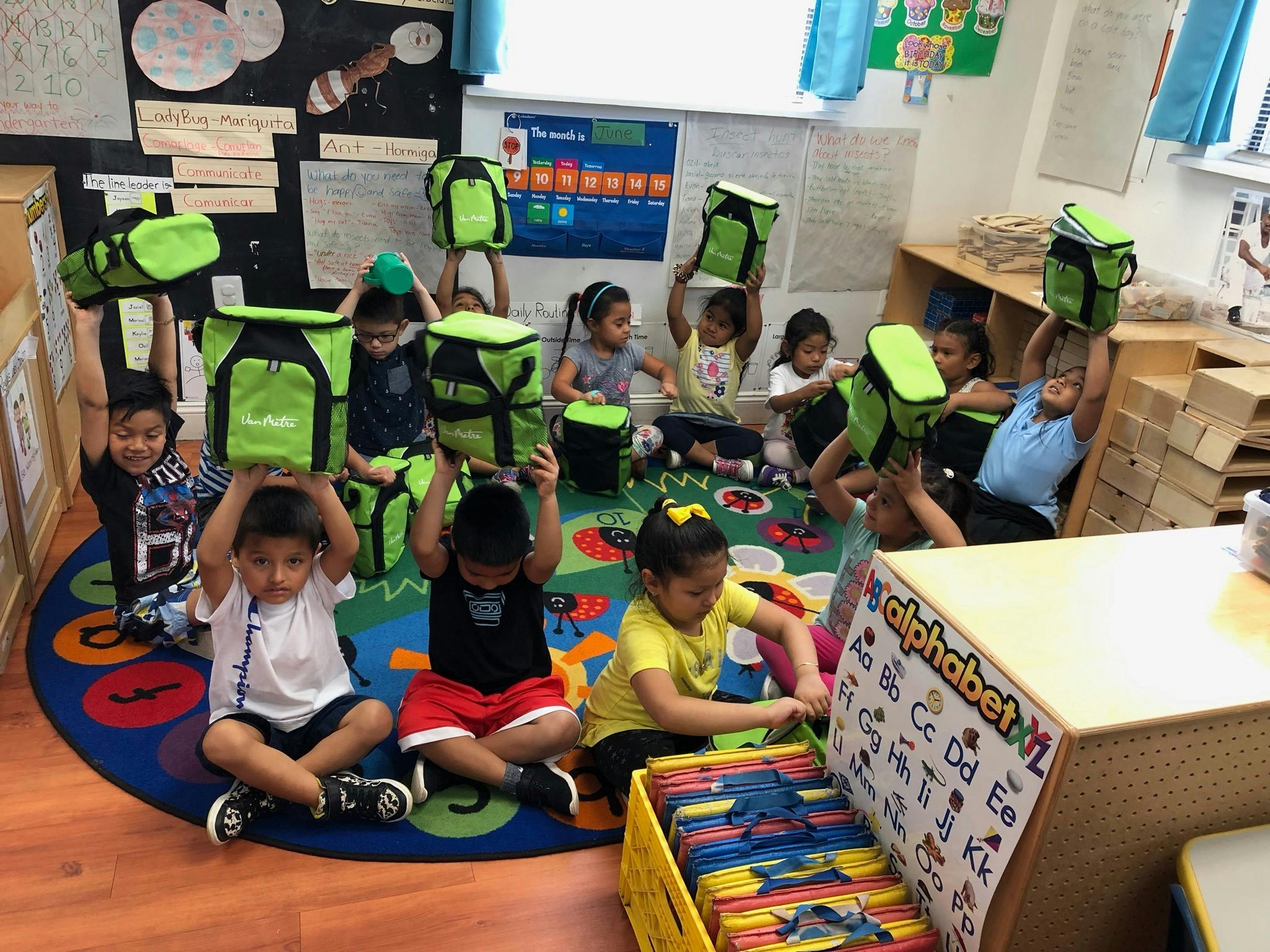 Children in a classroom holding up green lunch bags