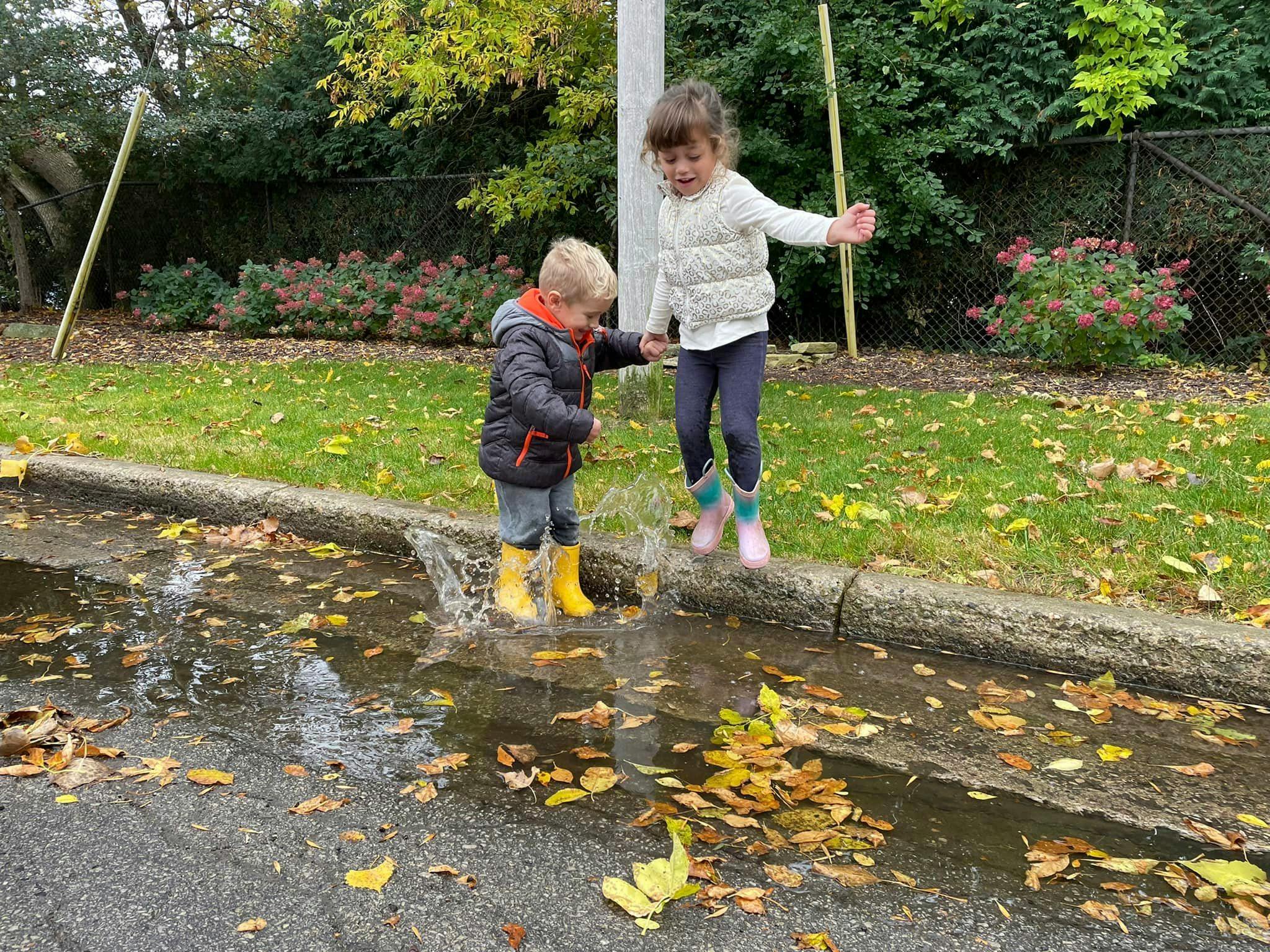 Two children playing in a puddle with autumn leaves