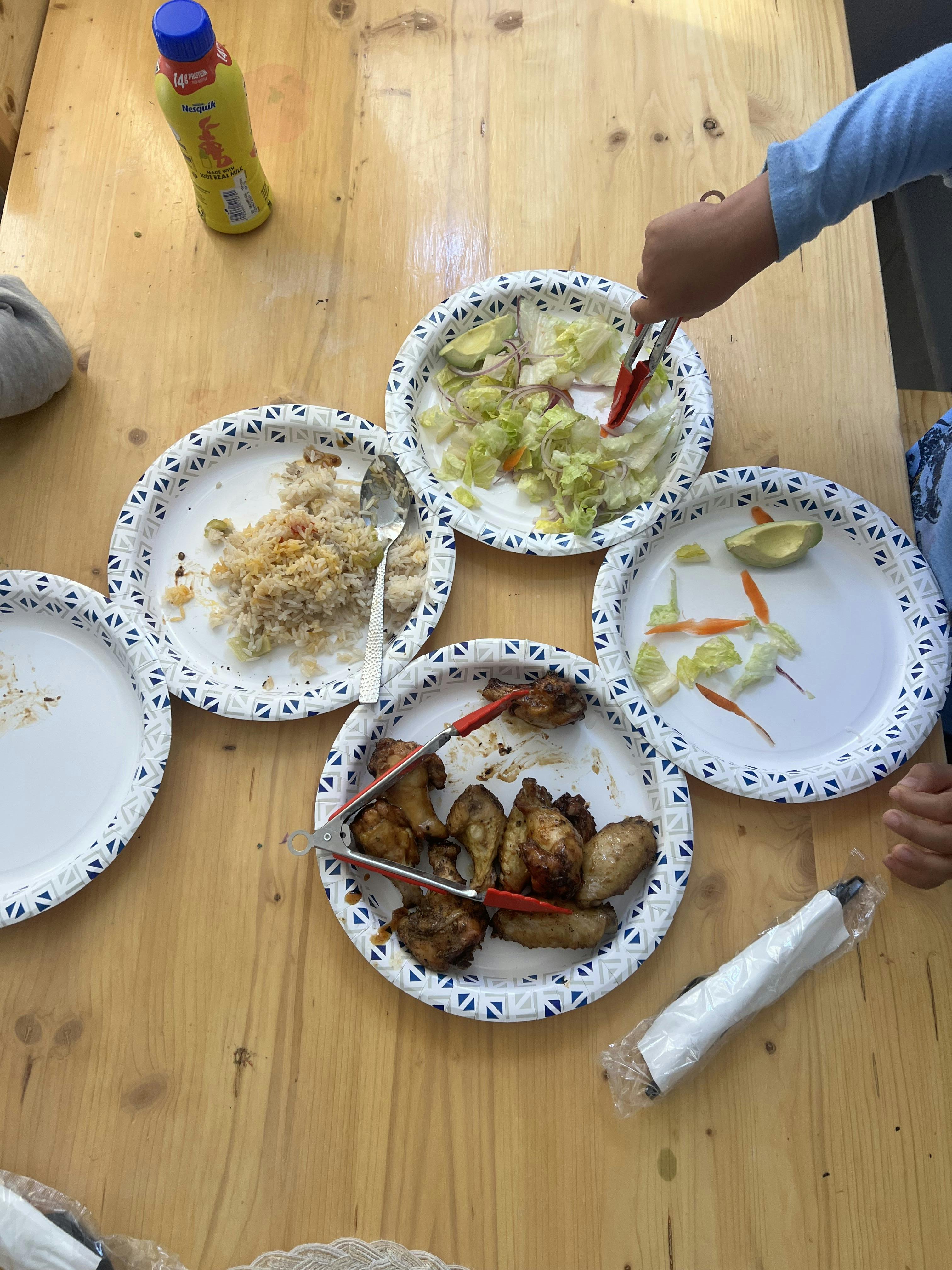 Child's hand serving salad onto a paper plate with tongs
