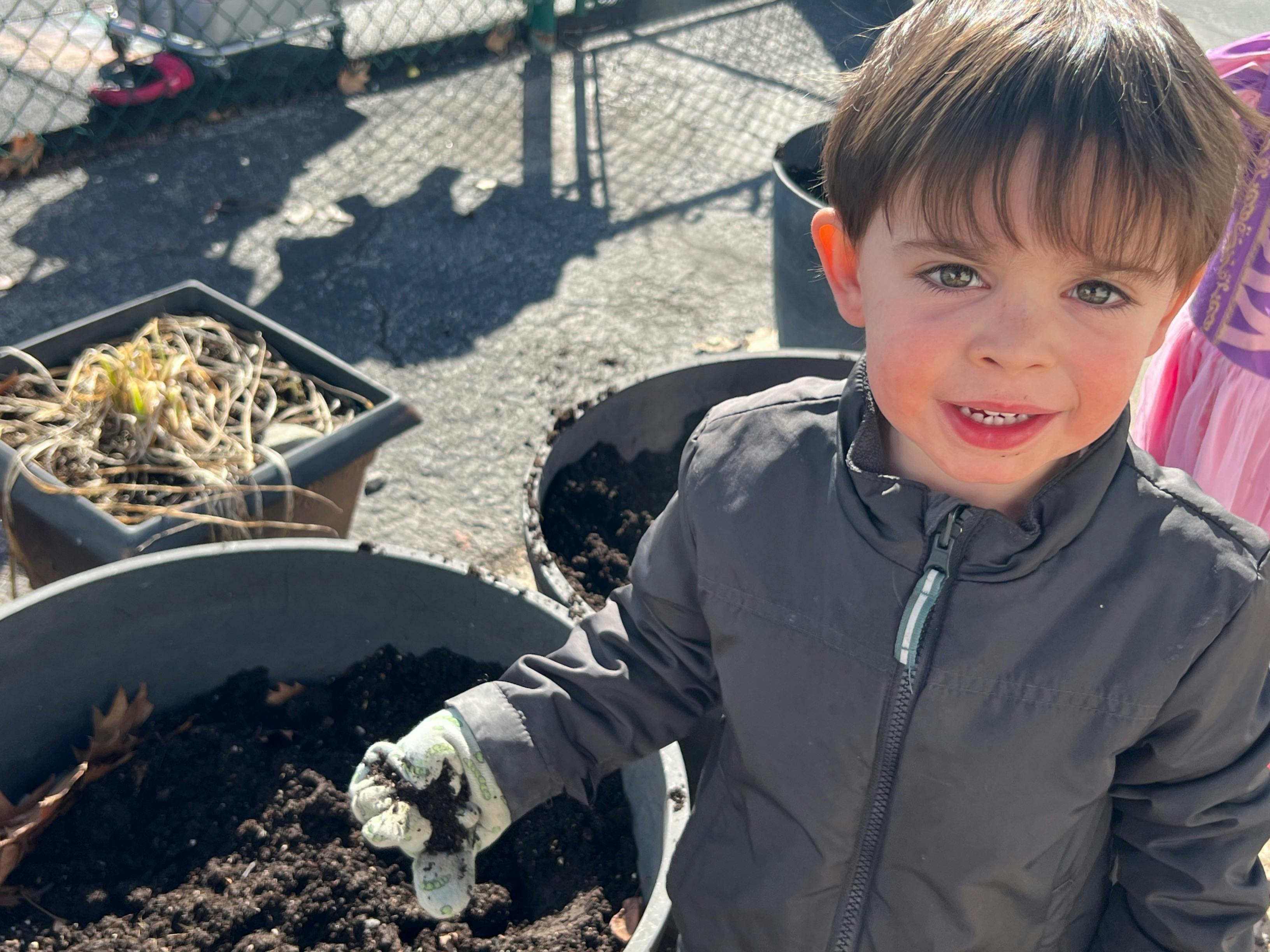Child wearing gloves and digging in dirt in a large planter