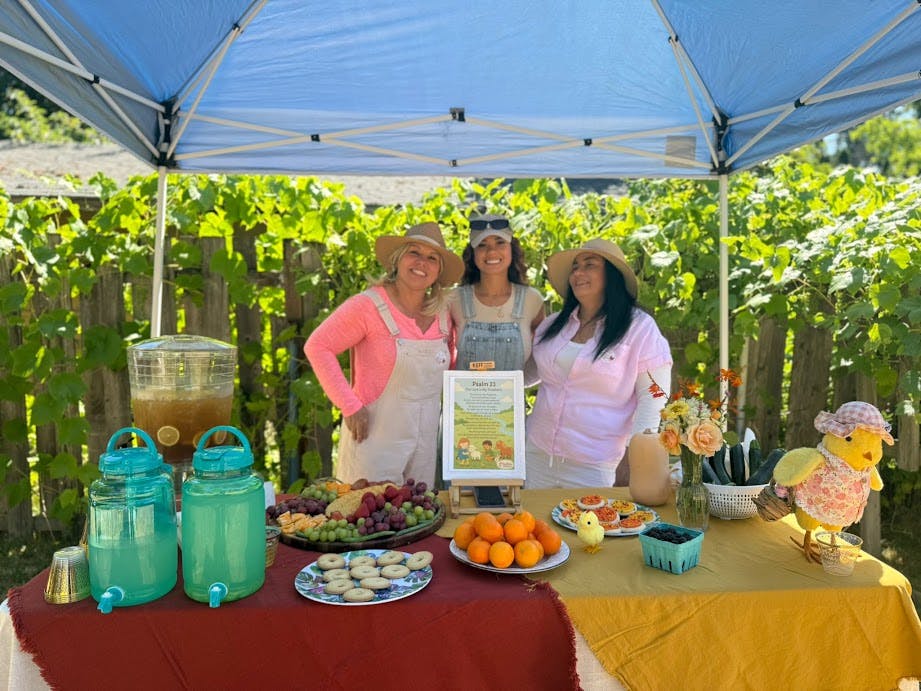 Three people standing behind a table with food and drinks under a canopy