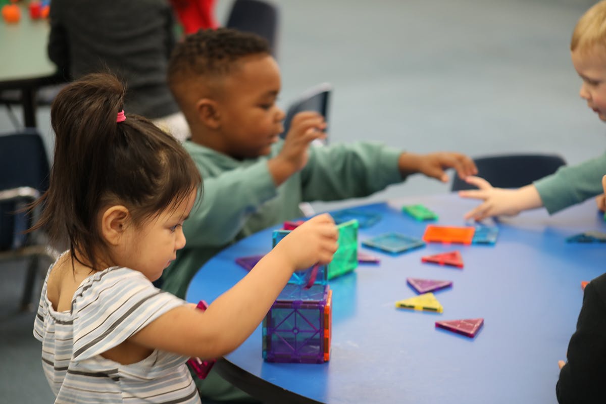 Children playing with colorful magnetic tiles at a blue table