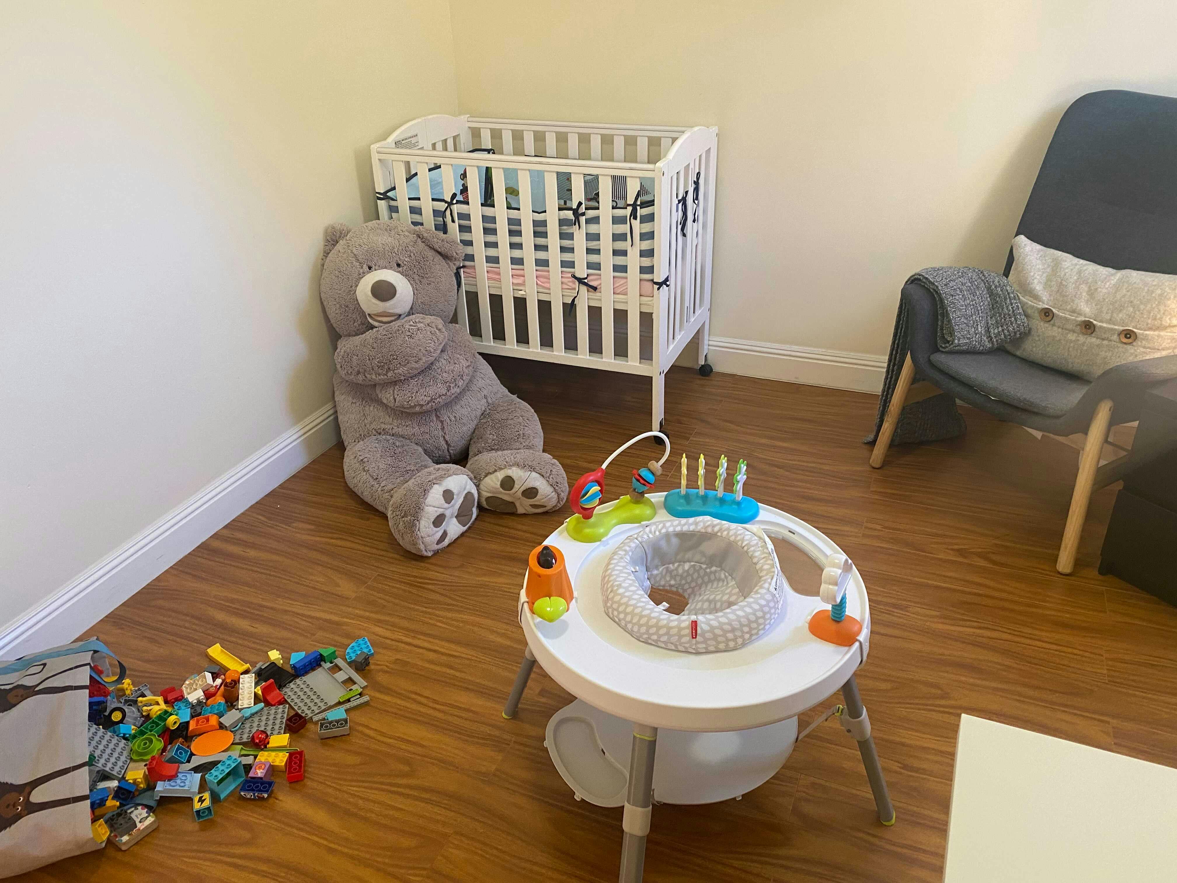 Baby crib, large teddy bear, and baby activity center in a room