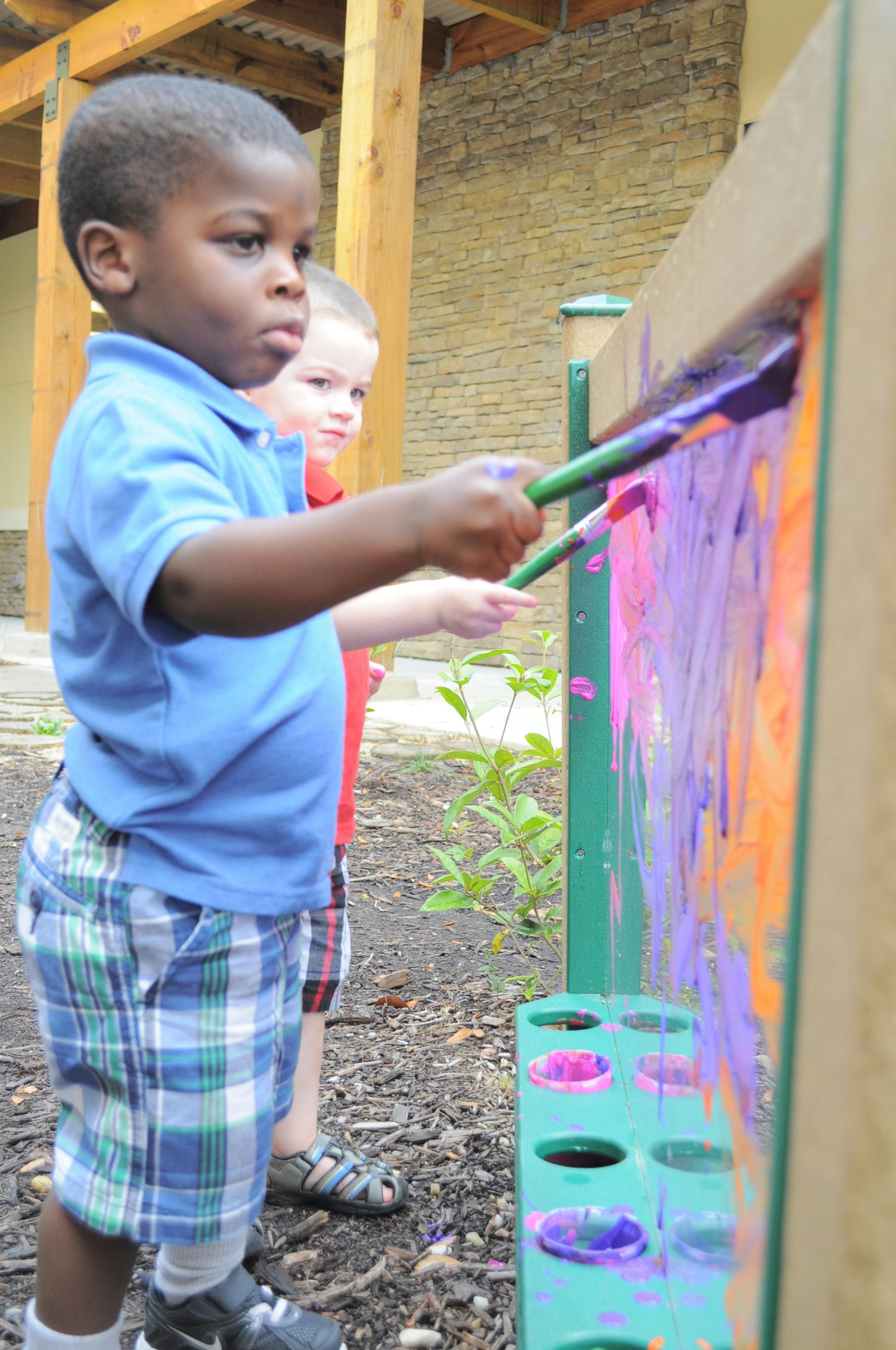Child painting on a clear board with another child nearby