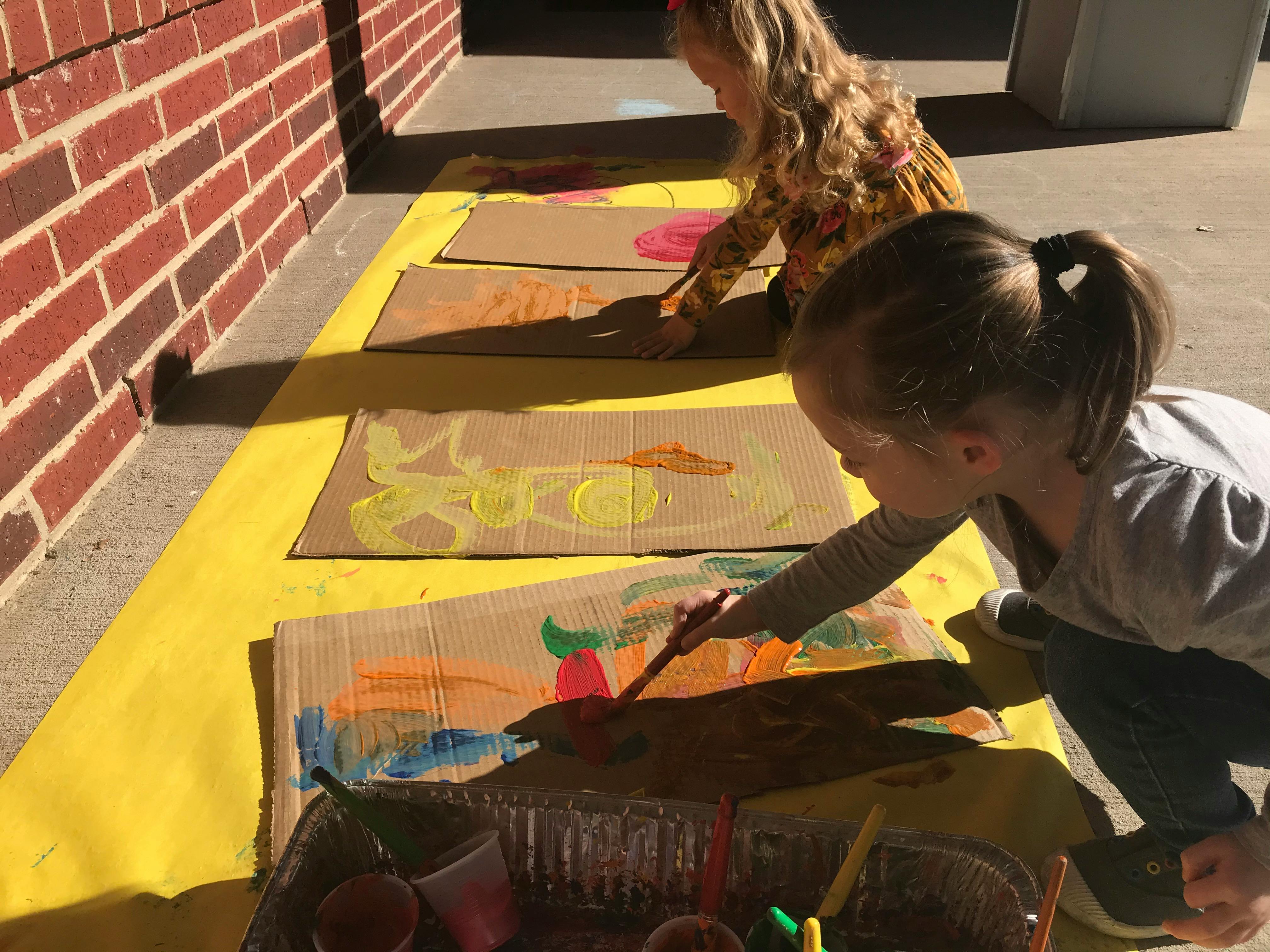 Two children painting on cardboard outside