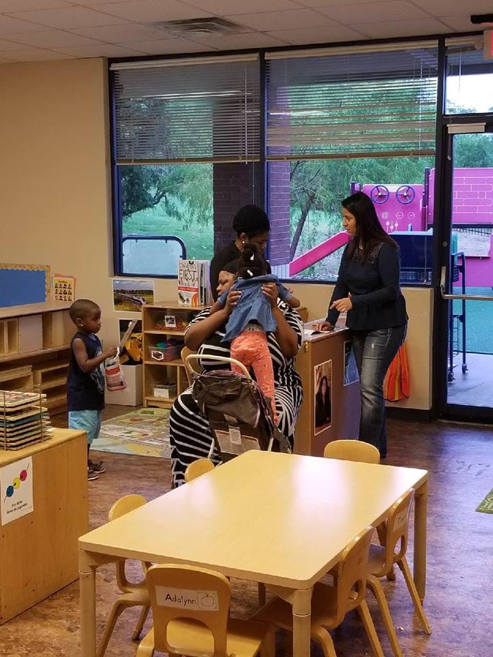 Three people in a classroom, one holding clothing, another standing by a desk