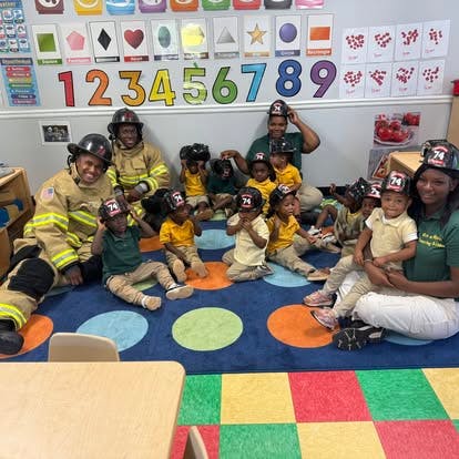 Firefighters visiting children in a classroom wearing helmets