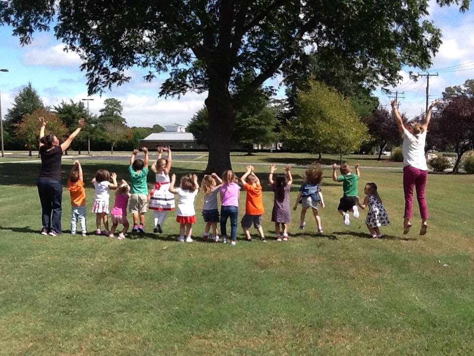 Adults and children jumping with arms raised outdoors