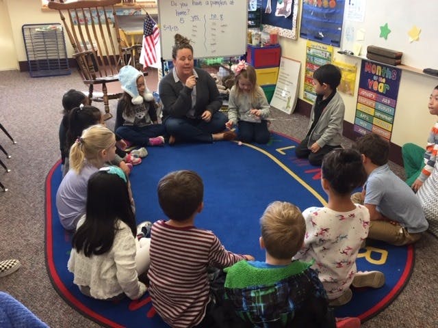 Adult and children sitting in a circle on a blue rug in a classroom