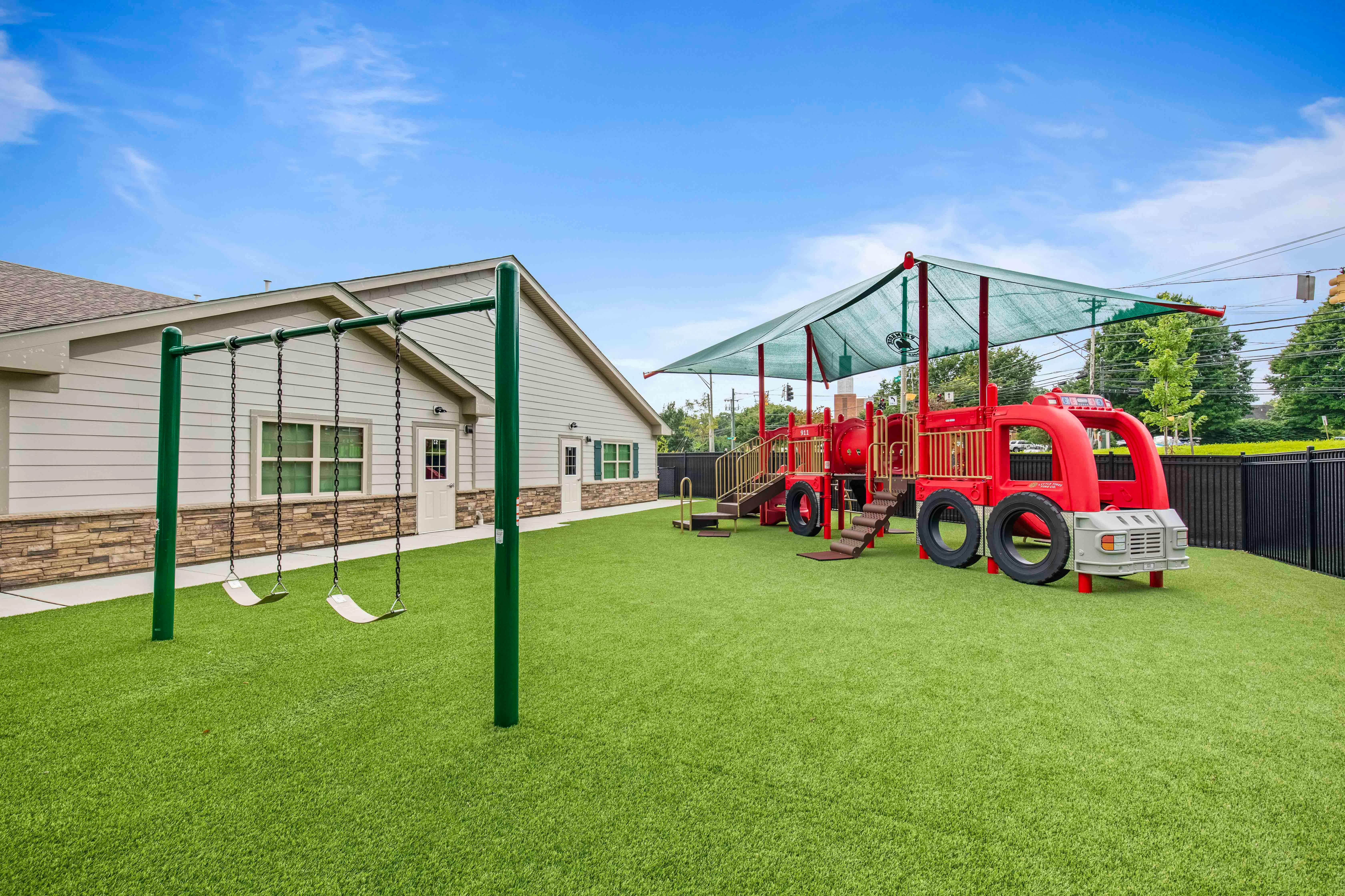 Playground with swings and a red fire truck shaped play structure on artificial grass