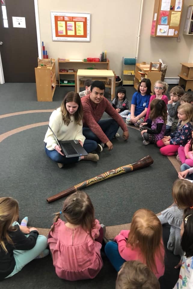 Two adults and several children sitting in a circle on the floor in a classroom