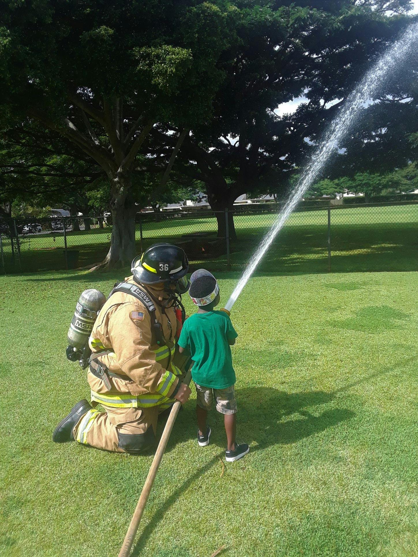 Firefighter kneeling with child holding a hose spraying water