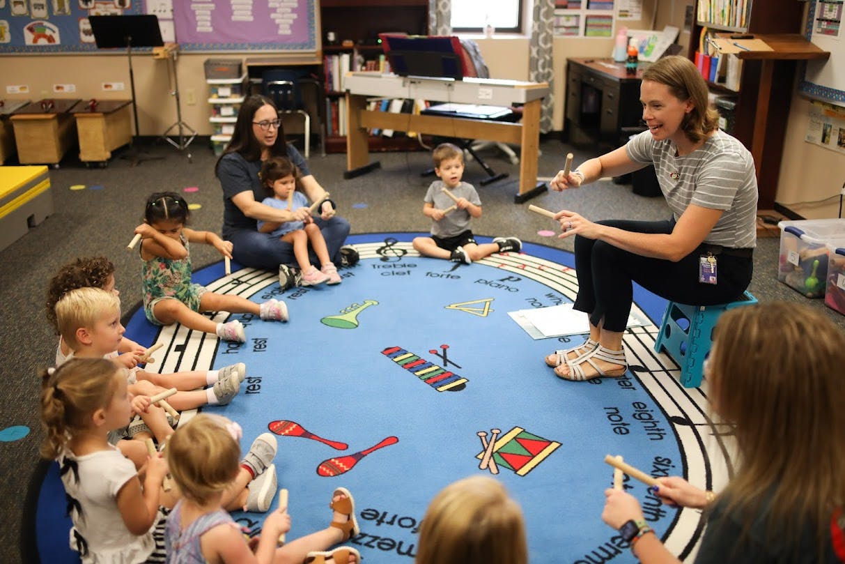 Adults and children sitting on a blue rug with musical notes and instrument designs
