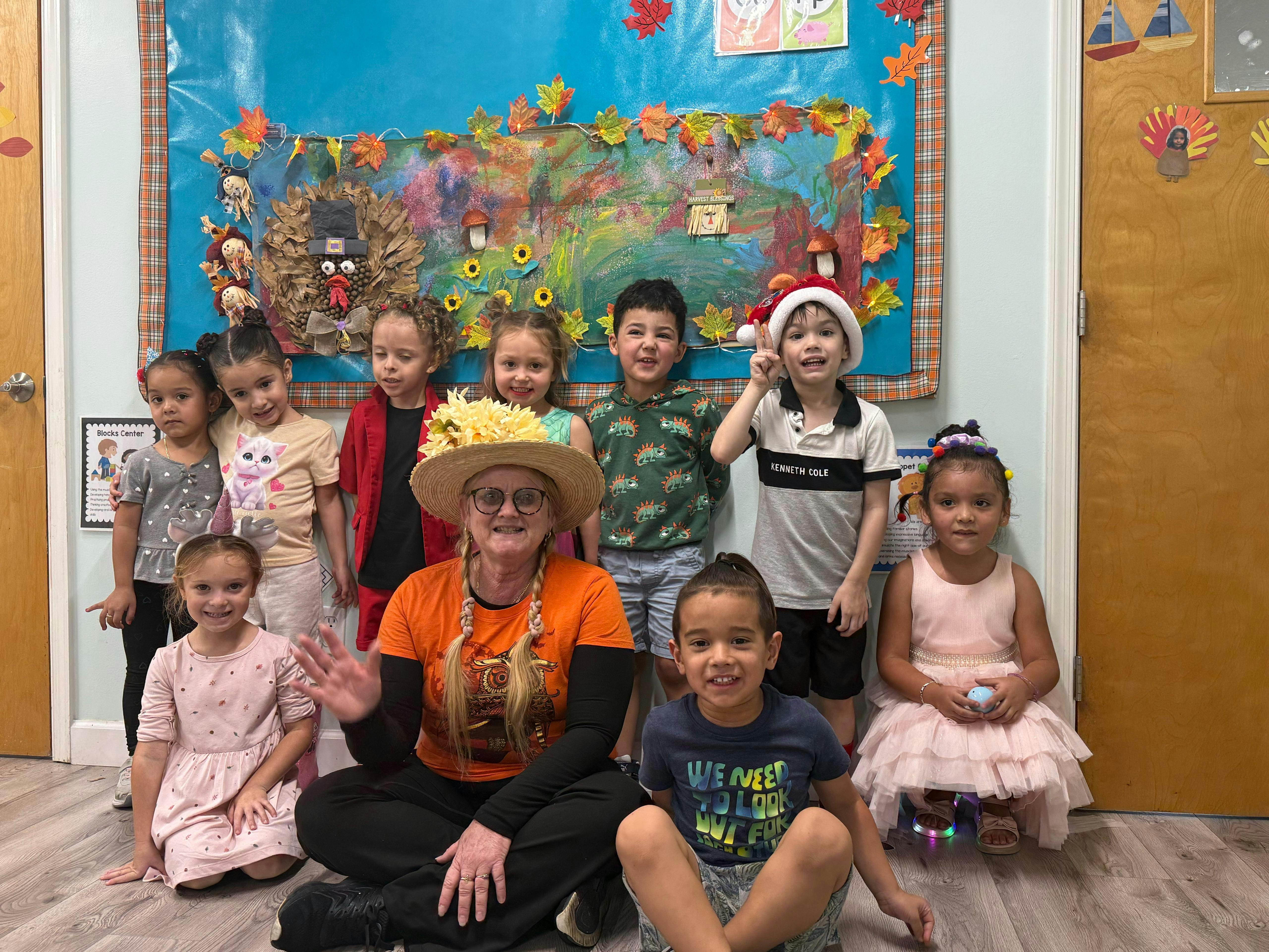 Adult and multiple children posing in front of a decorated bulletin board