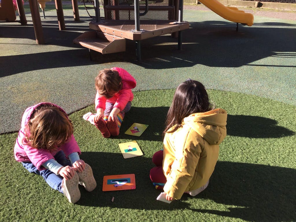 Three children sitting on artificial grass with books