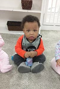 Child sitting on floor wearing a bib and holding a toy