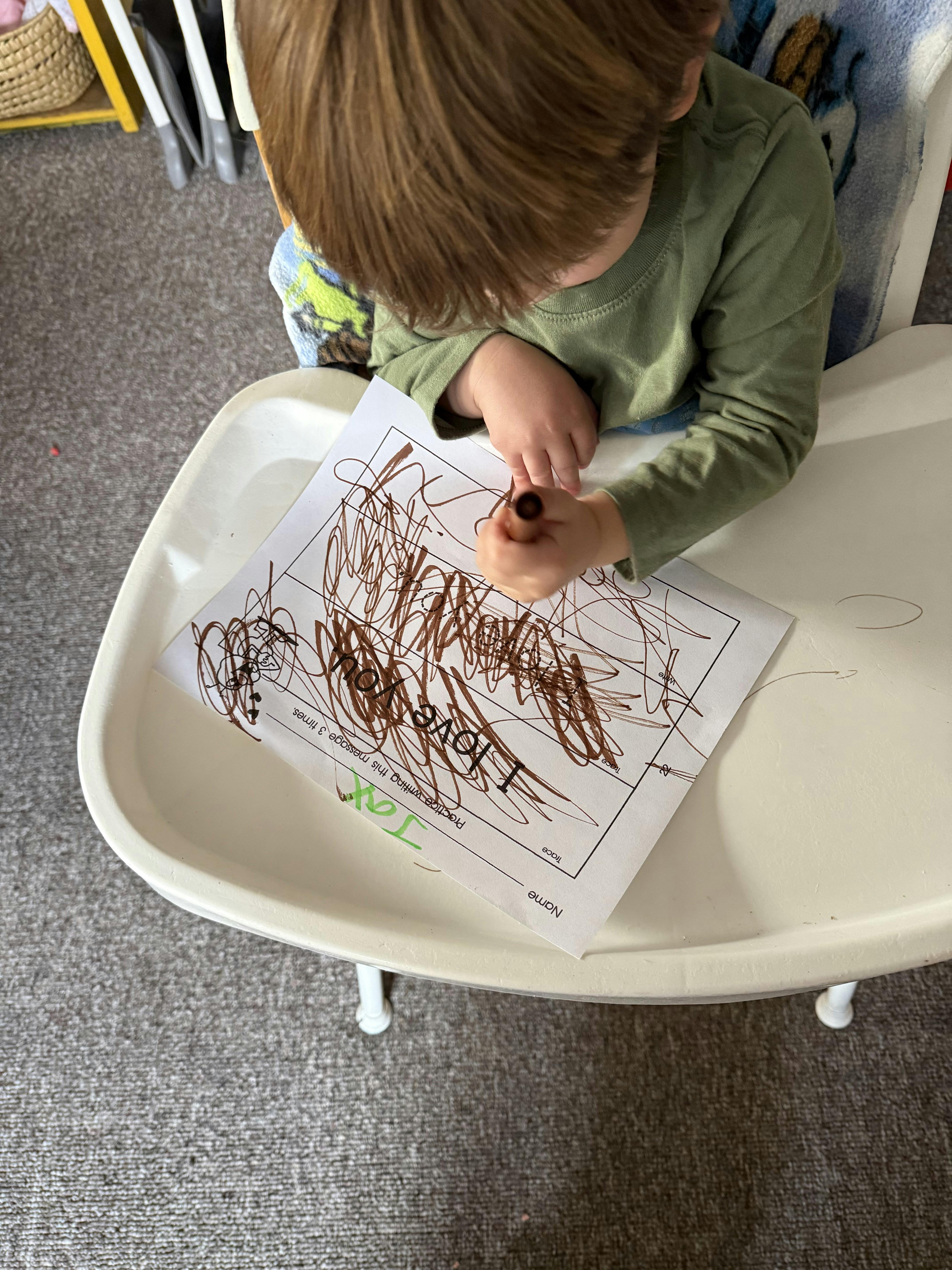 Child drawing on paper with a brown marker