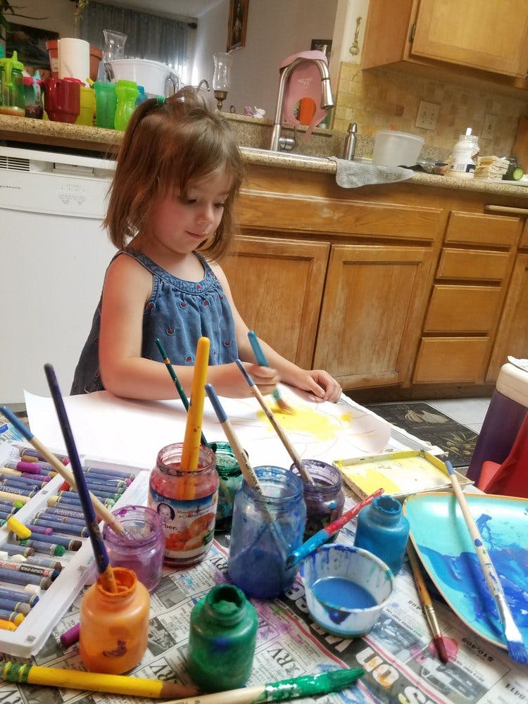 Child painting on paper with various art supplies on a table