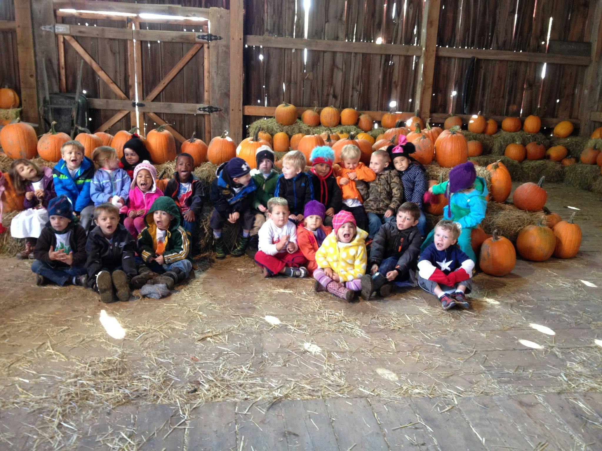 Group of children sitting on hay in a barn with pumpkins