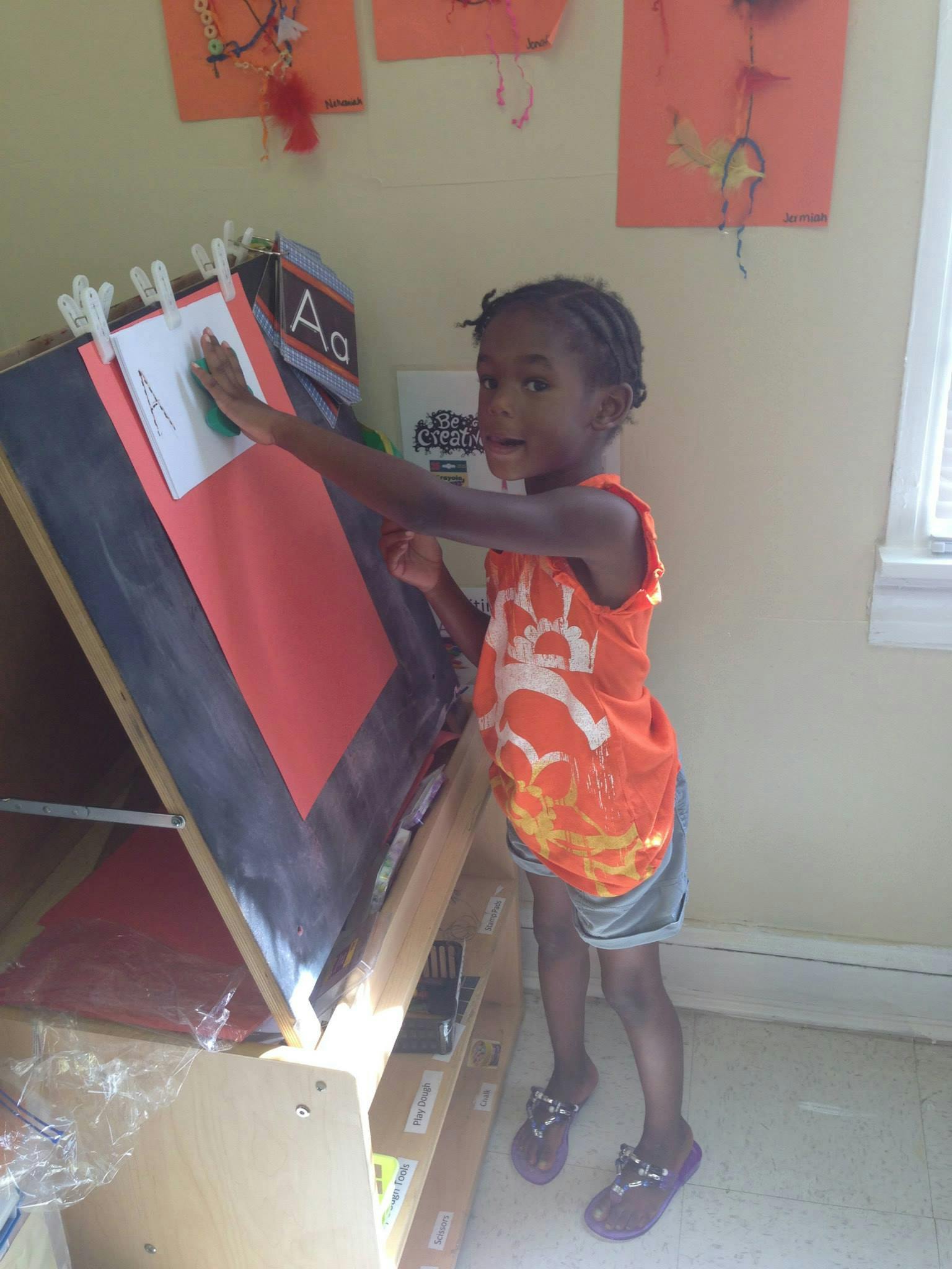 Child standing at an easel, reaching to touch a paper